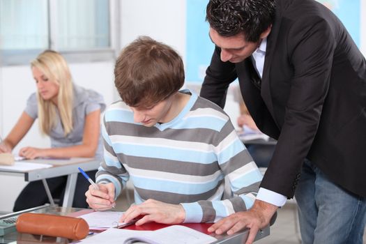 A teacher overlooking the work of one of his pupils in a classroom.