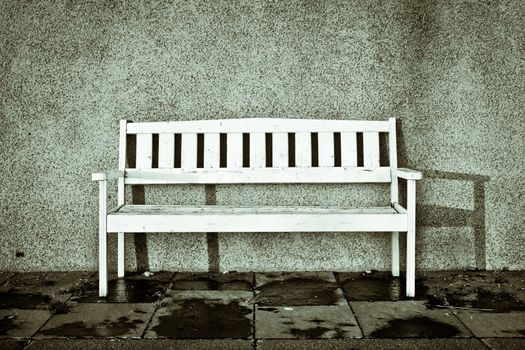A white bench on a town street with shadow from sunlight