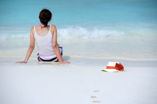 the hat is beside woman sitting on the beach and watching the sea