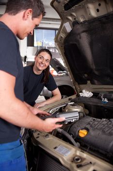 A man and a woman mechanic team doing service on a car in a garage
