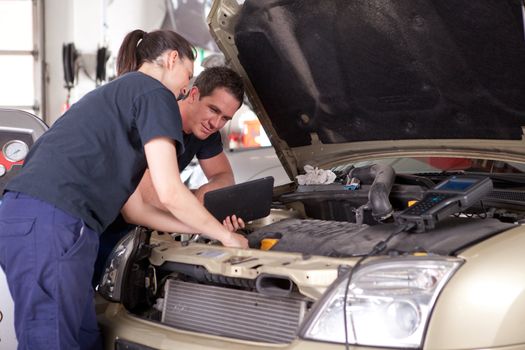 Man and woman team of mechanics using digital tablet while diagnosing car engine.