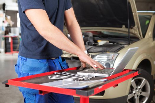 Mid section of mechanic working on laptop in a garage