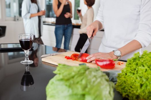 Cropped image of female cutting vegetables while friends having drink in background