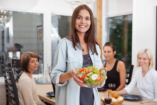 Portrait of happy female holding bowl of vegetables while her friends sitting in background