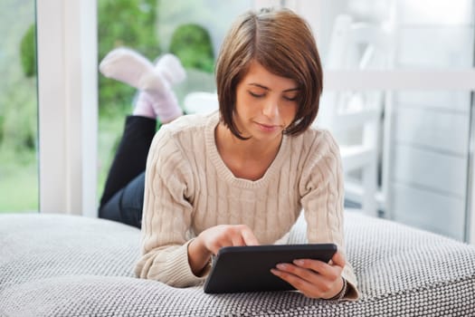 Pretty young woman using tablet pc while leaning on couch