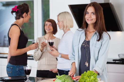 Portrait of pretty female cutting vegetables while her friends having drink in background