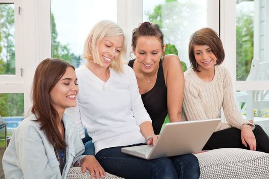 Group of smiling female friends sitting on couch and looking at laptop