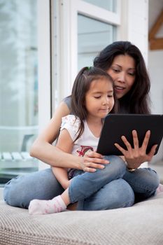 Happy mother and daughter using a digital tablet in a home interior, shallow depth of field with critical focus on child