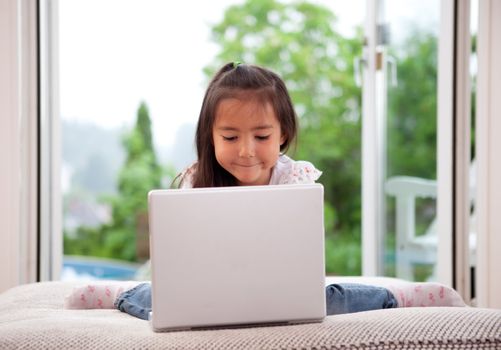 Young cute child using a computer in an indoor living room setting with large window