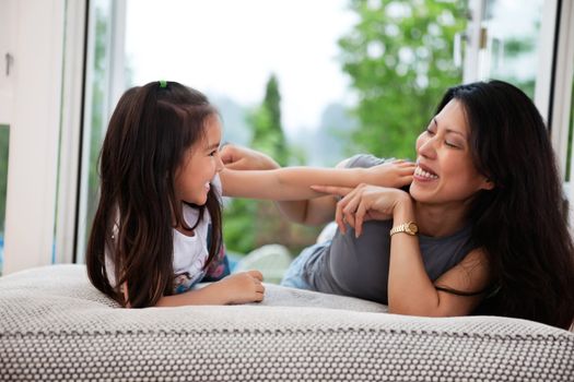 Portrait of happy mother and her daughter playing on couch