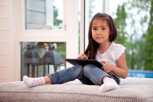 Happy young girl looking at the camera holding a digital tablet