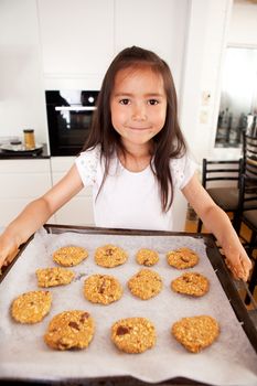 Cute young girl looking at camera with bakng sheet full of raw cookies