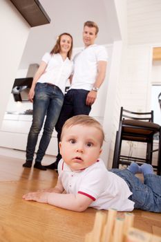 A child on the floor looking intently at the camera, parents in the background