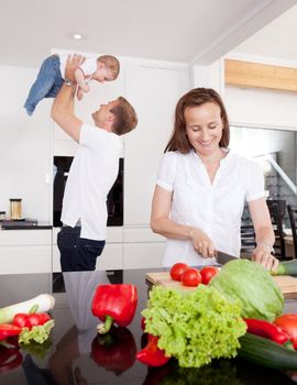A happy young family in the kitchen, mother preparing food and father playing with son