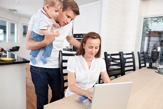 Father holding child while mother using laptop