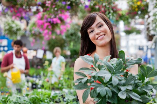 Attractive female customer holding potted plant with people in background