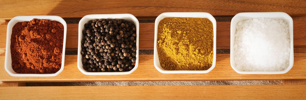 row of small bowls filled with spices from top on wooden background