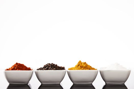 row of small bowls filled with pepper peppercorns curry and salt spices 