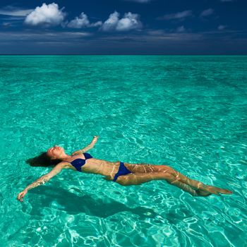 Woman in bikini lying on water at tropical beach