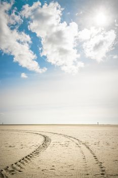 Tire tracks in the sand on the beach of St. Peter-Ording on a sunny day with blue sky and clouds