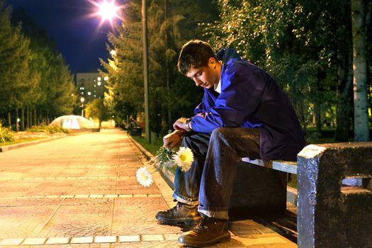 teenager with flowers sitting in the night park and looking on the watch