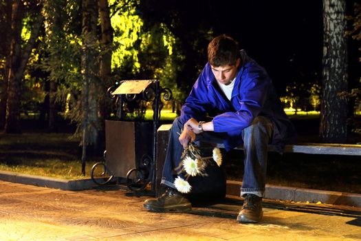 teenager with flowers sitting in the night park and looking on the watch