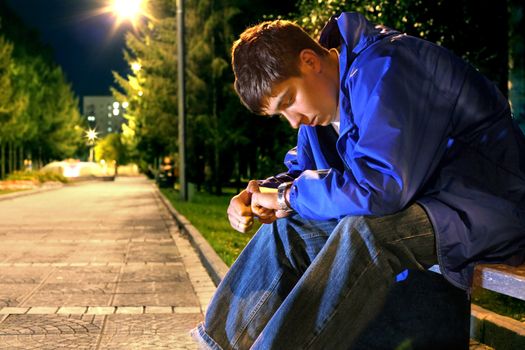 teenager sitting in the night park alley and looking on the watch
