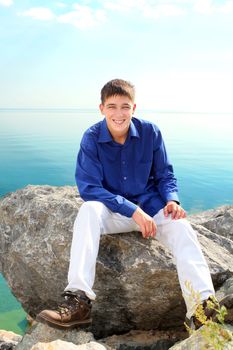 happy young man sitting on the rock near the water