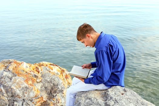 happy teenager sitting with a book on the stone on the seaside