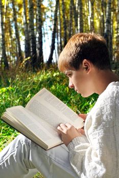 teenage boy sit in autumn forest with a book