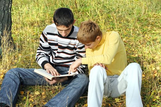 boys sit in autumn forest with a book