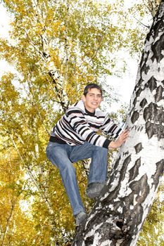 happy teenager climbing on the tree in the autumn forest