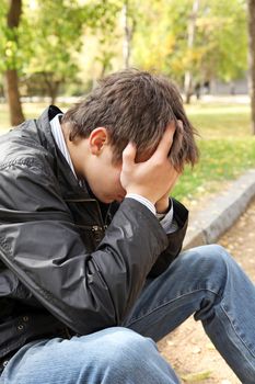 sad young man sitting in the autumn park