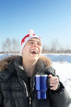 laughing young man in santa's hat with travel mug in the winter