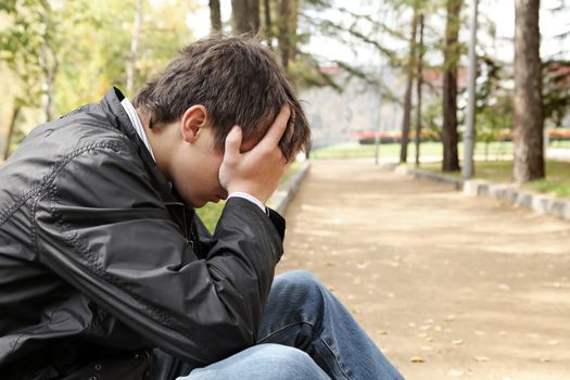 sad young man sitting in the autumn park