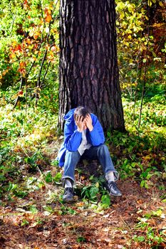 sorrowful teenager sitting in the autumn forest alone