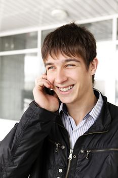 portrait of happy teenager with mobile phone near the glass building