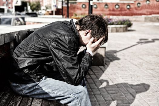 sorrowful young man sitting on the city street