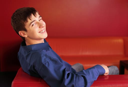 happy teenager sitting on the red sofa in home interior