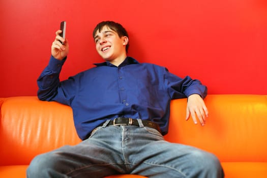 happy teenager with mobile phone sitting on the red sofa