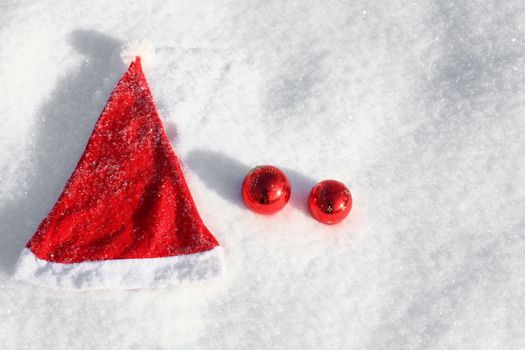 Santa's hat and two red christmass balls on the snow