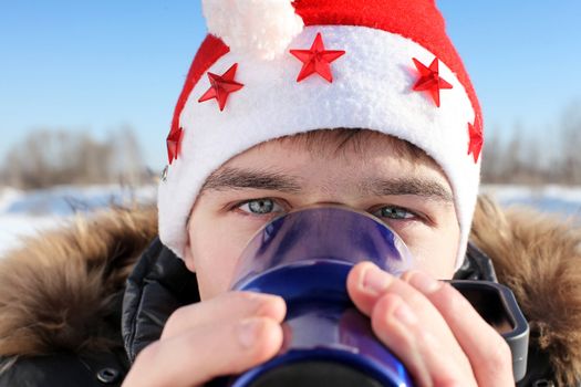 young man in santa's hat with travel mug in the winter