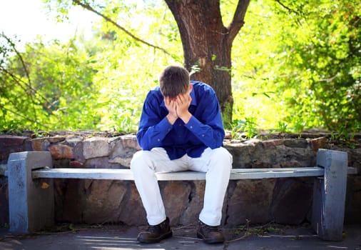 Sorrowful Young Man sitting on the bench in the Summer Park