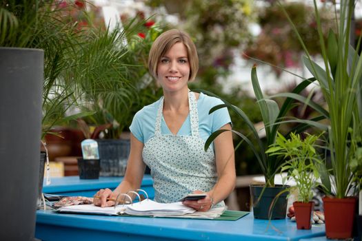 Portrait of a happy greenhouse employee writing in a log book and looking at the camera