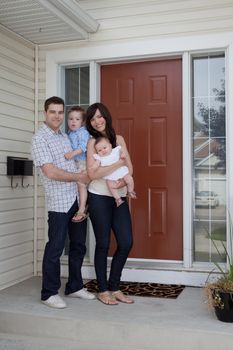 Portrait Of Sweet Family Standing In Front Of Their House.