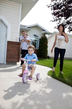 Little boy learning to ride tricycle while parents watch