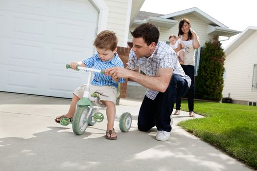 Father teaching his son to ride tricycle while wife standing in background