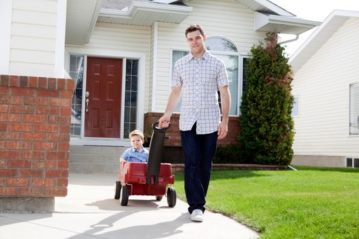 Father pulling son in a wagon in front of house on sidewalk