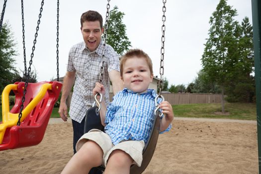 Happy father pushing boy on swing in playground