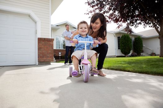 Beautiful happy young mother teaching her son to ride bike